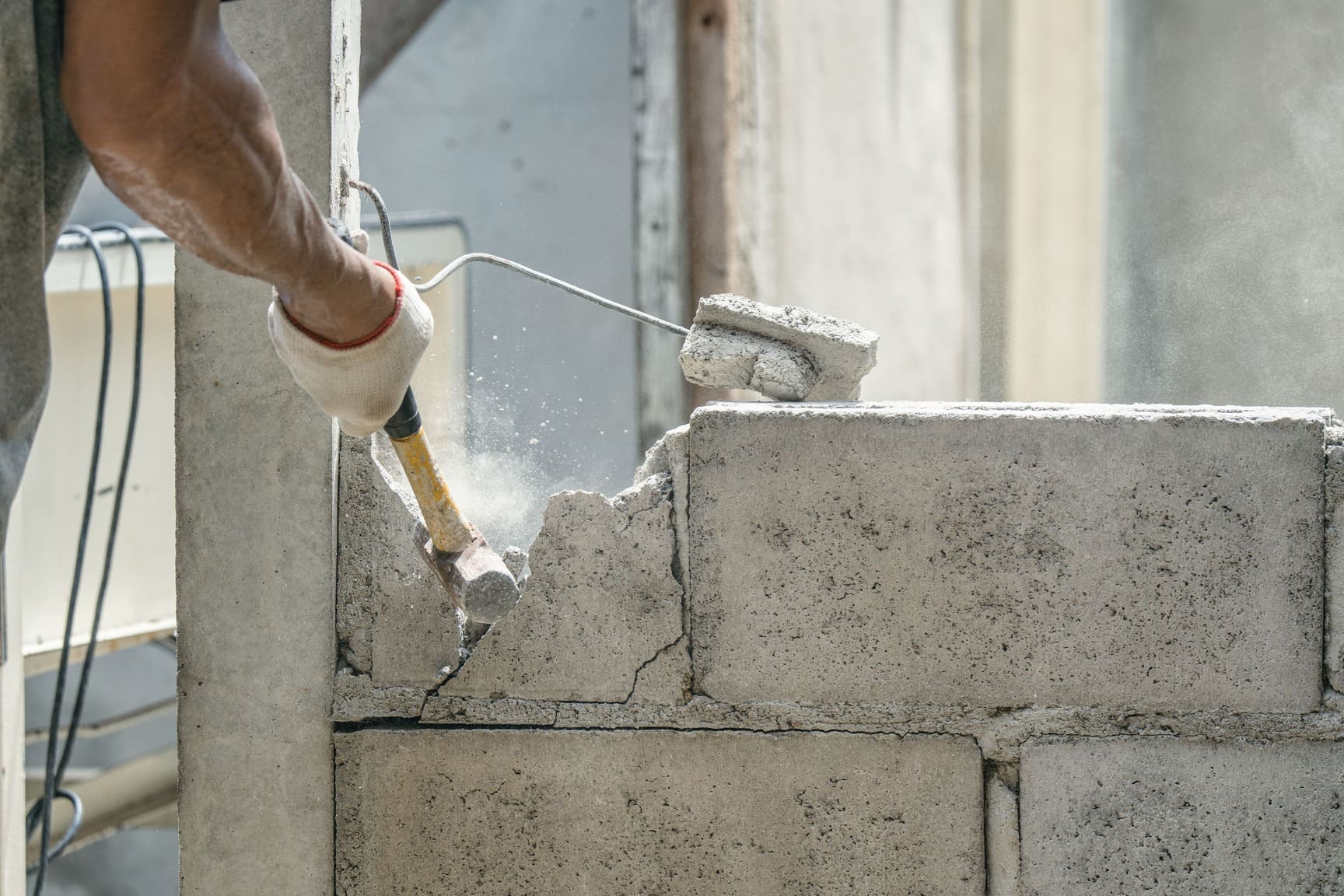 Démolition d'un mur en parpaing par un technicien avec un marteau
